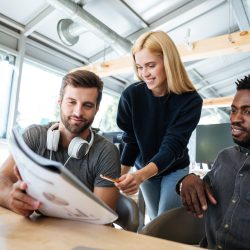 Image of happy young colleagues in office coworking using laptop computers and talking with each other. Looking aside.
